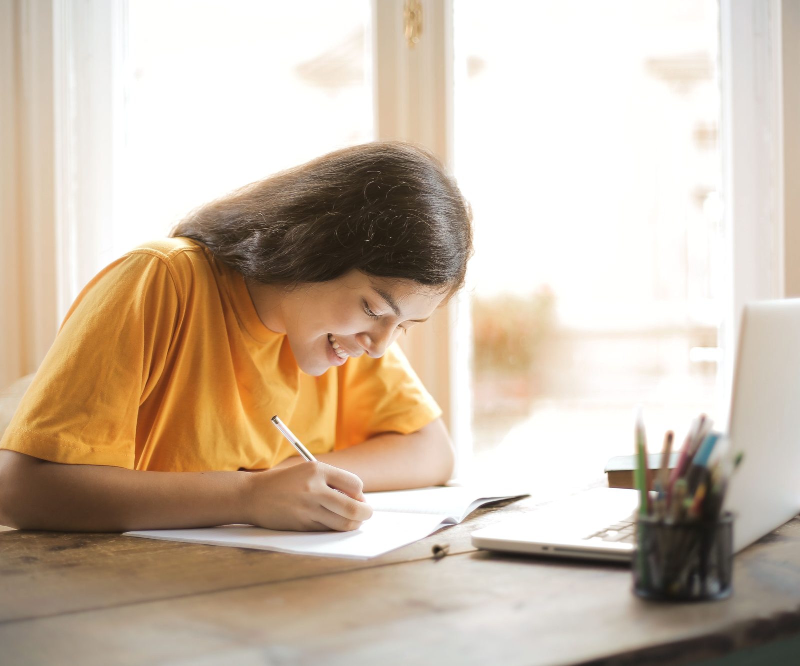 Smiling student writing in a notebook next to her laptop during an online tutoring session